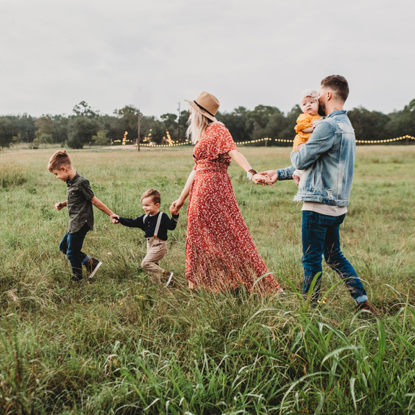 family of two parents and three young children walking hand-in-hand through a field