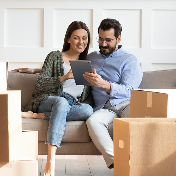 couple requesting an insurance quote on their tablet while sitting on the sofa amidst moving boxes